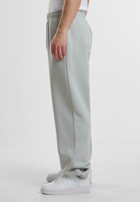Hellgraue Jogginghose mit elastischem Bund und Seitentaschen, entspannter Schnitt und weichem Material, kombiniert mit weißen Turnschuhen.