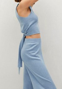 Top corto de punto azul claro con un detalle atado en la cintura, combinado con pantalones de pierna ancha a juego. Textura suave, diseño ajustado y estilo casual.