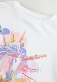 Camiseta blanca con un diseño colorido de unicornio adornado con lentejuelas de color rosa dorado y detalles florales, que presenta una textura suave y cuello redondo.
