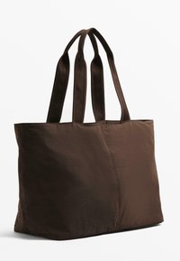 Brown fabric tote bag with two long, sturdy handles, featuring a simple design and slightly wrinkled texture. No visible hardware.