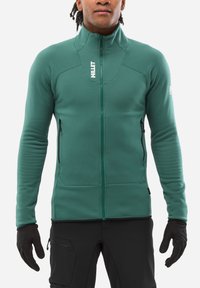 Grüne Fleecejacke mit vollem Reißverschluss, hohem Kragen und zwei Reißverschlusstaschen. Aus elastischem Material und mit tailliertem Schnitt für mehr Beweglichkeit.