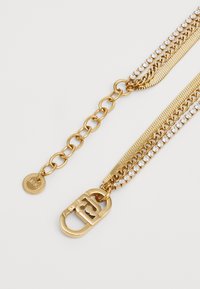 Gold multi-chain necklace featuring rhinestone accents, a textured chain, and a clasp with logo detailing. Round tag for branding included.