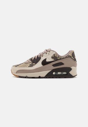 Sneakers Nike Air Max 90 v béžovej farbe s hadím vzorom. Vyznačujú sa čiernym swooshom a vzduchovým jednotkovým systémom, doplnené svetloružovými šnúrkami.