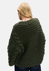 Gruby zielony sweter z dzianiny z teksturowanym wzorem warkocza na rękawach i szerokim dekoltem, wykonany z grubej przędzy dla zapewnienia ciepła.