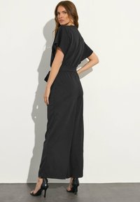 Tuta nera con vestibilità comoda, maniche corte, vita elastica e design a gamba larga. Tessuto liscio e dettagli minimi.