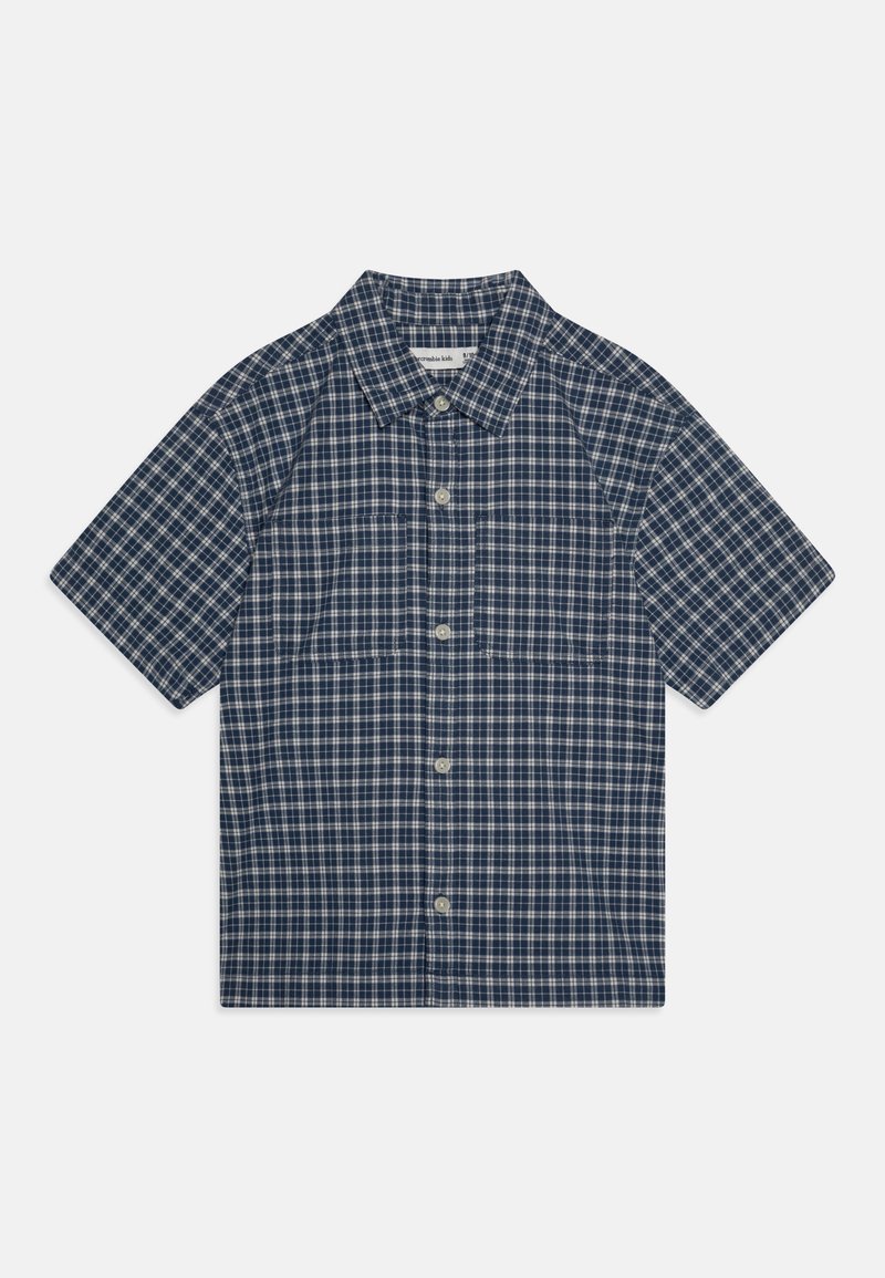 Kék és fehér kockás, rövid ujjú pamut ing. Gombolható gallérral és elülső gombokkal rendelkezik. Egyenes szabású, laza illeszkedésű.