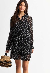 Black floral dress with long sleeves, collar, and tiered design. Made of sheer fabric with white and light blue flower patterns.