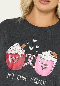 Czarny t-shirt z grafiką dwóch kubków gorącej czekolady, jeden czerwony i jeden różowy, z serduszkami, laseczkami cukrowymi i bitą śmietaną.