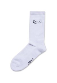 Weißer Sportsocken in Knöchellänge mit schwarzem, kursivem Logo nahe der Oberseite und schwarzen Zahlen in der Nähe der Spitze, flach auf weißem Hintergrund liegend.