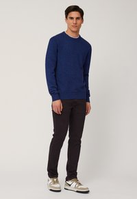 Maglione testurizzato blu navy con colletto a girocollo, abbinato a pantaloni scuri e sneakers bianche con accenti beige e neri.