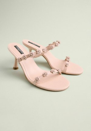 Šviesiai rožiniai aukštakulniai šlepetės su gėlių papuošimais ant dirželių, tekstūruota pado danga ir lieknas kulnas.