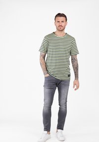 Camiseta verde a rayas con líneas negras, escote redondo, corte holgado. Llevada con jeans gris desgastados y zapatillas blancas.