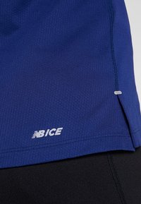 Närbild av blått atletiskt tyg med "NB ICE"-logotyp och synliga sömmar på sidokanten över en svart tygbakgrund.