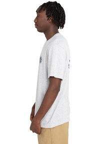 Graues Baumwoll-T-Shirt mit kurzen Ärmeln, das ein kleines blaues Grafikdesign auf der linken Brust und zusätzliche Grafiken auf dem Rücken aufweist.