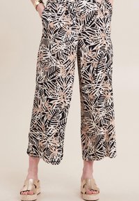 Zwart-witte wijde broek met een botanische bladerenprint in metallic rosegoud, voorzien van zijzakken en een casual pasvorm. G gedragen met gouden platform sandalen.