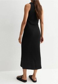 Robe midi noire à côtes avec un design sans manches et une silhouette cintrée, associée à des sandales noires avec des boucles dorées.