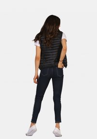 Gilet en duvet noir avec un motif matelassé horizontal, associé à un jean foncé avec des rayures sur les côtés et des chaussures slip-on blanches.