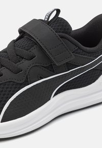 Chaussure de sport noire avec tige en maille et accents texturés. Elle comprend une sangle Velcro, un col rembourré, une semelle blanche et des détails contrastants.