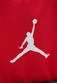 Σιλουέτα παίκτη μπάσκετ που πηδάει με το ένα χέρι τεντωμένο, κρατώντας μια μπάλα μπάσκετ, πάνω σε κόκκινο φόντο με υφή.