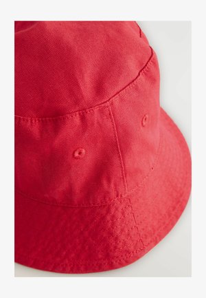 Piros pamut vödörkalap, textúrált felülettel, kerek koronával, széles peremmel és varrott részletekkel. Oldalán szellőzőnyílásokkal rendelkezik.