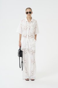 Set di due pezzi bianco ricamato con dettagli a traforo; camicia ampia a maniche corte, pantaloni a gamba larga, borsa nera e occhiali da sole.