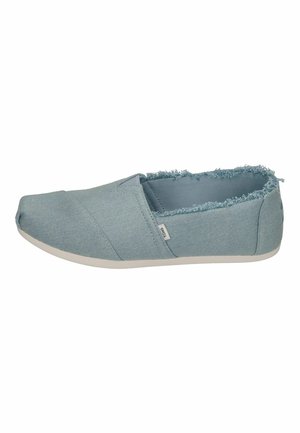 Baskets en toile bleue à enfiler avec bords effilés, bout rond et semelle en caoutchouc blanche. Comprend une étiquette sur le côté et un tissu texturé.