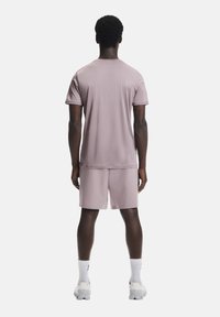 Vaaleanpunainen urheilut-paita, joka on yhdistetty vastaaviin shortseihin. Pehmeä, hengittävä kangas, lyhyet hihat ja rento istuvuus.