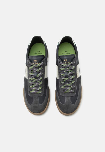 Ζευγάρι σκούρα γκρι και λευκά sneakers με κορδόνια, πράσινες λεπτομέρειες και καφέ σόλες, από πάνω σε λευκό φόντο.