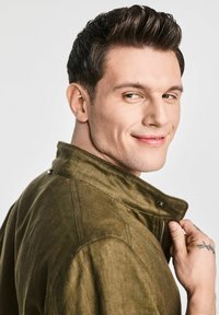 Jacket w kolorze oliwkowym, o fakturowanej powierzchni, z kołnierzem stójkowym, zapięciem na zamek oraz zatrzaskami, noszony przez modela w luźnej pozie.