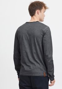 Graues Langarmshirt aus einem weichen, strukturierten Stoff mit Rundhalsausschnitt und genähten Akzenten. Verfügt über ein kleines braunes Markenlabel am Saum.