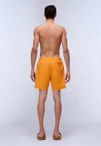 Shorts de bain orange avec une taille élastique ; doté d'une petite poche arrière. Le matériau semble léger avec une texture lisse.