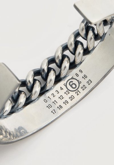 Κοντινή λήψη ασημένιας αλυσίδας βραχιολιού με μεταλλική πλάκα που φέρει αριθμούς 0–23, με το 6 να είναι κυκλωμένο.
