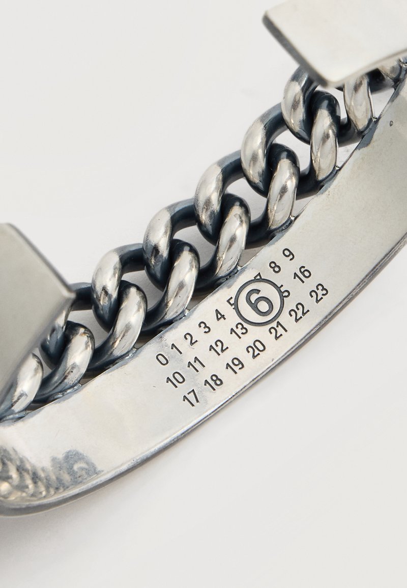 Gros plan d'un bracelet en chaîne argentée avec une plaque métallique affichant les chiffres de 0 à 23, le chiffre 6 étant encerclé.