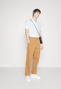 Vit polo t-shirt med korta ärmar och broderad logga, matchad med lösa bruna byxor och vita sneakers. Svart crossbody-väska.