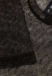 Tessuto nero trasparente con piccoli punti testurizzati, caratterizzato da una finitura liscia e un motivo sottile. Include una zona del collo con dettagli neri.