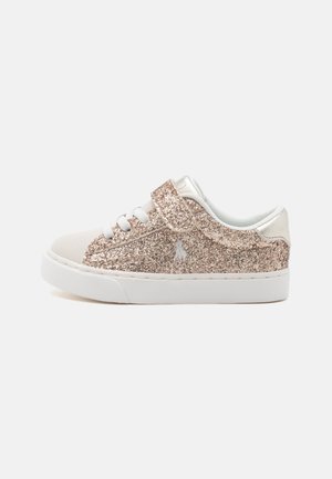 Lavtop børnesneaker med hvid sål, gyldent glitteroverdel, hvide snørebånd og velcrorem på en ensfarvet baggrund.