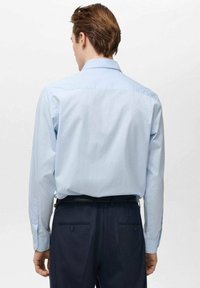 Camicia a righe azzurro chiaro con colletto abbottonato, maniche lunghe e una texture liscia, abbinata a pantaloni scuri. Dettagli dei bottoni visibili.
