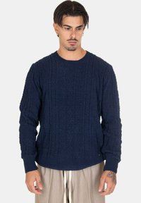 Maglione lavorato a maglia blu navy con motivo a trecce, scollo a girocollo e polsini a coste. Realizzato in tessuto testurizzato, presenta maniche lunghe e una vestibilità comoda.
