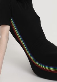 Svart ribbad klänning med en flerfärgad regnbågsrand längs sidan, som visar en jämn textur och en åtsittande design.