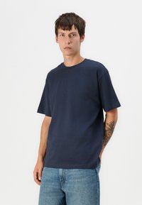 Marineblaue Baumwoll-T-Shirt mit Rundhalsausschnitt, kurzen Ärmeln und lockerer Passform. Verfügt über eine glatte Textur und ein minimalistisches Design.