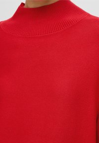 Roter Strickrollkragenpullover mit geripptem Kragen und strukturierter Oberfläche, der ein glattes, enges Gewebe im gesamten Kleidungsstück betont.