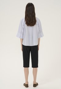 Camicia azzurra a maniche corte con dettagli sulla schiena, abbinata a pantaloni neri a tre quarti e scarpe basse verde oliva. Tessuto dalla consistenza liscia.