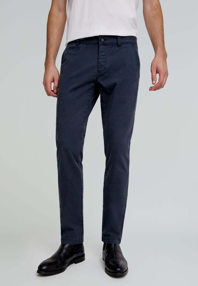 Marineblauwe chinos van katoen, met een recht model, voorzakken en een knoopsluiting, gecombineerd met zwarte enkellaarzen.