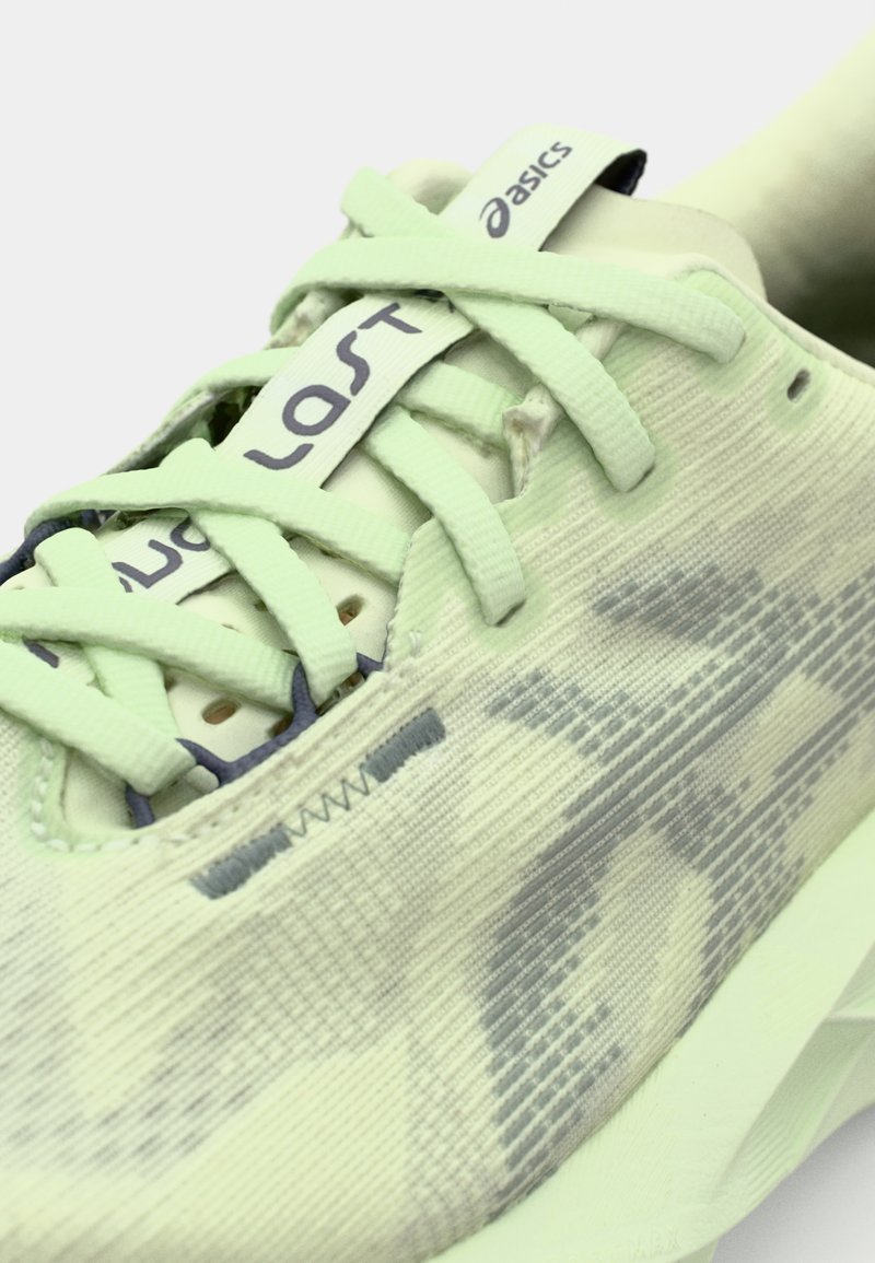 Scarpa da corsa verde chiaro con tomaia in mesh, motivo tonale, linguetta imbottita e lacci piatti. Presenta un logo e accenti a contrasto in blu navy.