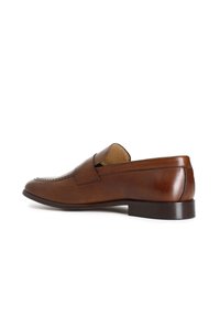 Scarpa slip-on in pelle marrone con tacco basso, punta arrotondata e cuciture decorative sopra la tomaia. Finitura liscia con una texture opaca.