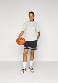 Camiseta de manga corta gris claro, pantalones cortos negros con franjas blancas, calcetas blancas y zapatillas coloridas. Sosteniendo un balón de baloncesto.