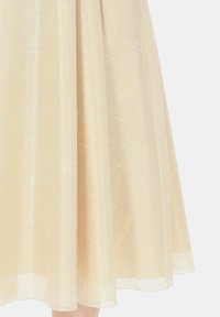 Spódnica o średniej długości wykonana z lekkiego, połyskującego materiału. Posiada subtelną, prążkowaną strukturę w jasnym beżowym kolorze oraz miękką, zwiewną teksturę.