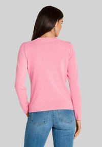 Figurbetontes Langarm-Sweatshirt aus weichem, hellpinkem Material mit einem runden Ausschnitt; kombiniert mit blauen Jeans, die eine glatte Textur und minimale Nähte aufweisen.