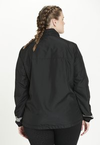 Svart vindjacka med hög krage, elastiska ärmar och reflexdetaljer vid ärmarna. Slätt, lätt material.