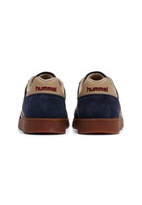 Marina mocka sneakers med beige detaljer, gummisulor och en röd "hummel"-logotyp på hälen. Texturerad ovandel med kontrasterande material.